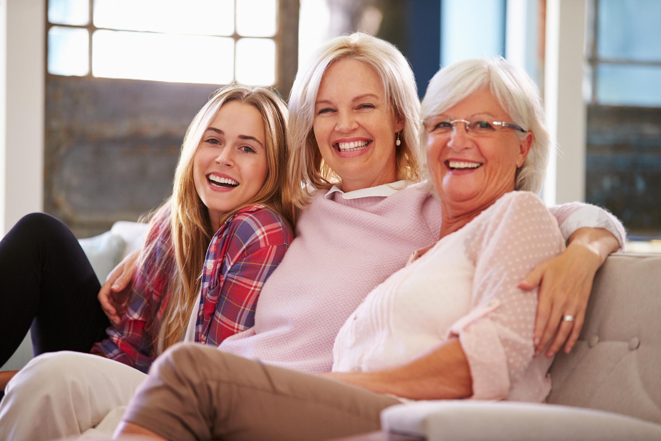 Grandmother With Mother And Adult Daughter Relaxing On Sofa, Smiling To Camera